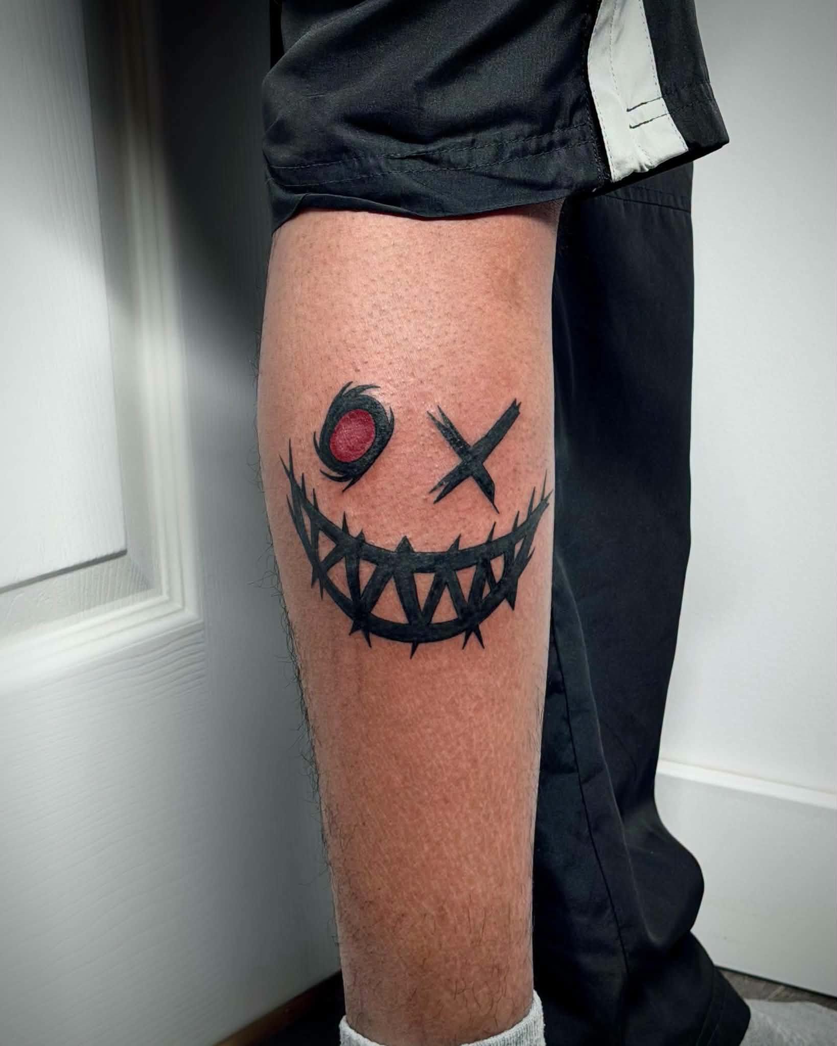 Blackwork thorn smile face tattoo on leg